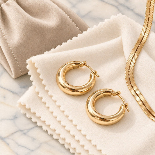 Gold hoop earrings and herringbone chain on a soft polishing cloth with a jewelry pouch
