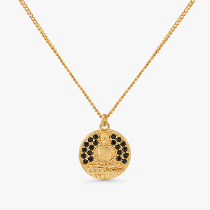 A gold pendant necklace featuring a circular medallion with a seated Buddha figure, accented by small black stones around the upper half, suspended from a delicate gold chain against a light gray background.