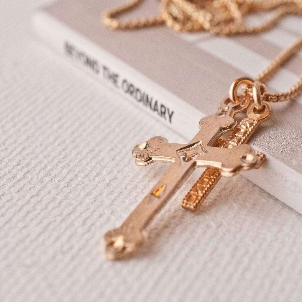 Rose gold cross pendant necklace with a textured crucifix design and matching chain, styled on a textured white surface next to a book.