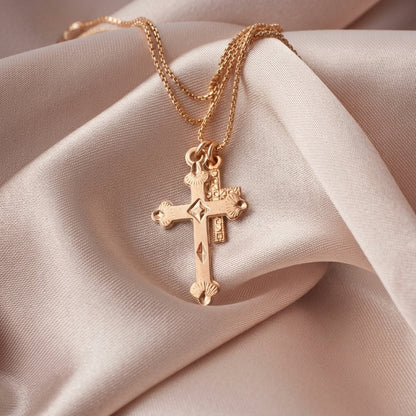 A gold cross pendant necklace with a small crucifix charm, displayed on draped champagne-colored satin fabric.