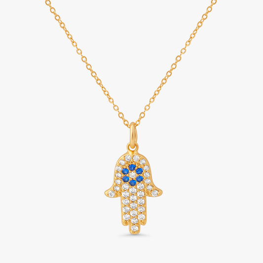A gold Hamsa hand pendant necklace adorned with clear crystals and blue gemstones, suspended from a delicate gold chain against a light gray background.