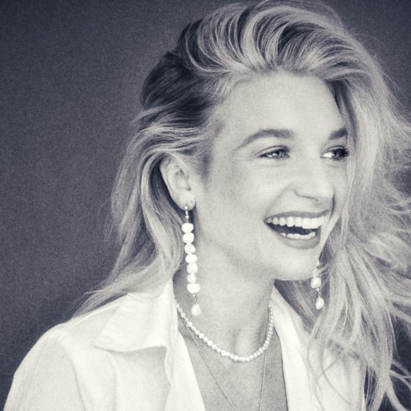 Black and white photo of a smiling woman wearing long 14k Gold Filled freshwater pearl drop earrings and a pearl necklace.