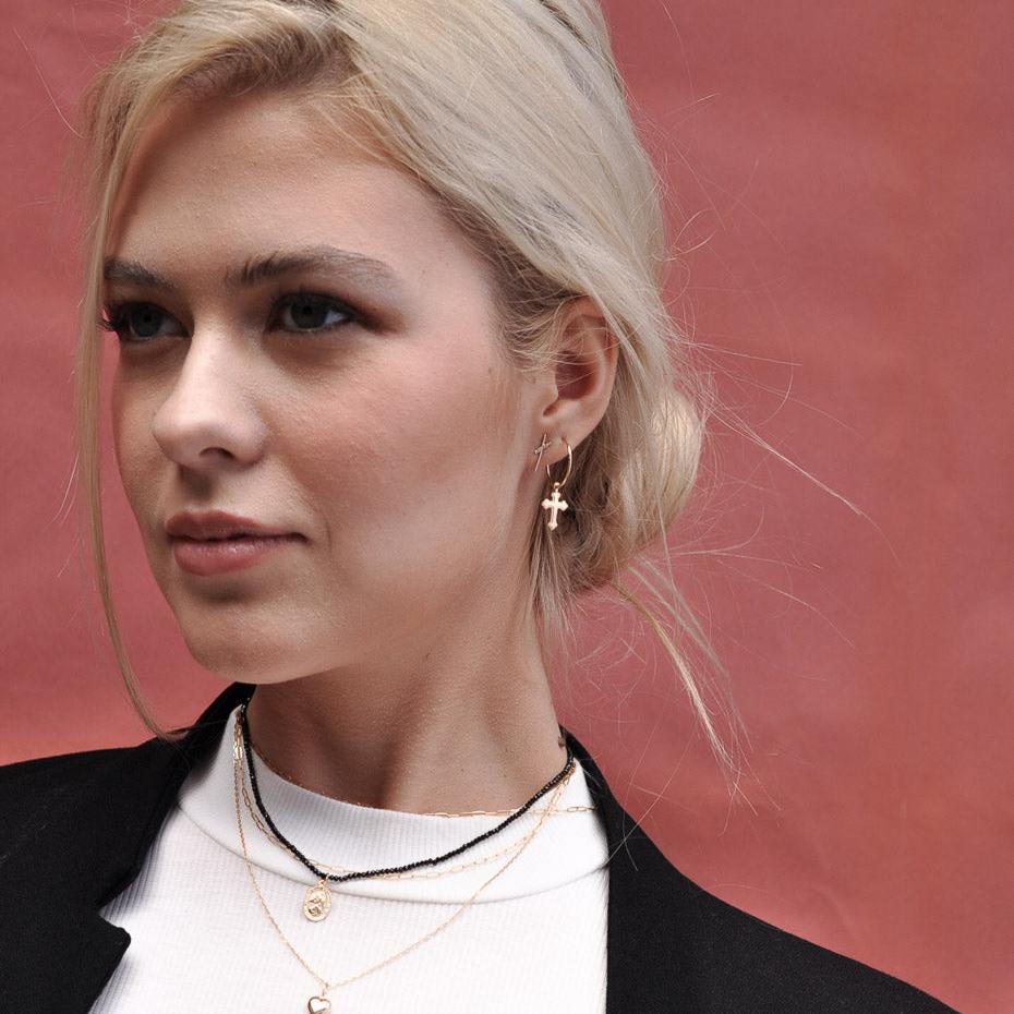 Blonde woman posing in a blazer wearing a 14k Solid Gold cross charm hoop earring.
