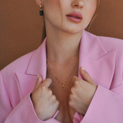 Blonde woman wearing Lykke Lucky Wishbone 14k gold filled necklace holding lapels of pink blazer