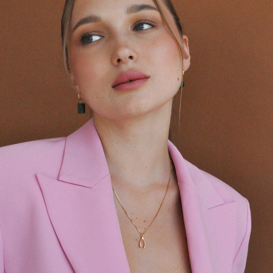 Blonde woman wearing Lykke Lucky Wishbone 14k gold filled necklace in pink blazer looking off-camera