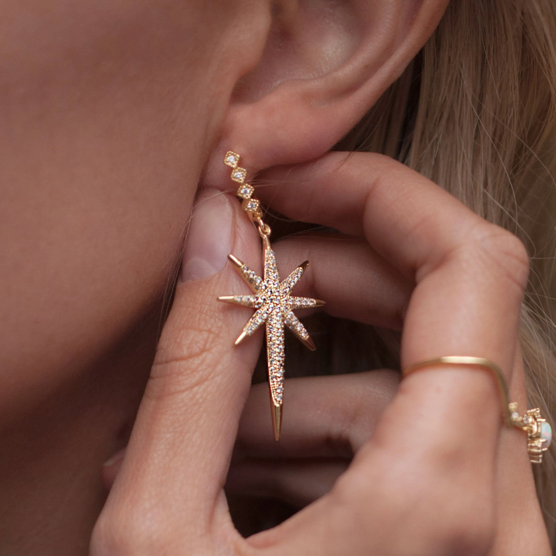 Close-up of model holding a gold starburst drop earring with crystal accents.