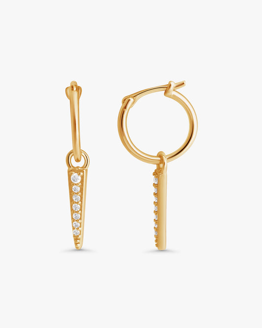 A pair of gold hoop earrings with a vertical bar and small clear stones, shown on a light gray background.