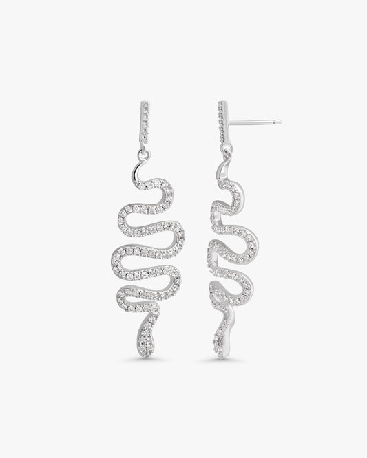 A pair of silver drop earrings with a wavy, snake-like spiral design set with small clear stones, shown against a plain light gray background.