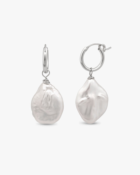 A pair of sterling silver hoop earrings with large, irregular white baroque pearl drops, shown against a light gray background.