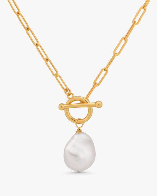 A gold chain necklace with a toggle clasp and a single baroque-style white pearl pendant, shown against a light gray background.