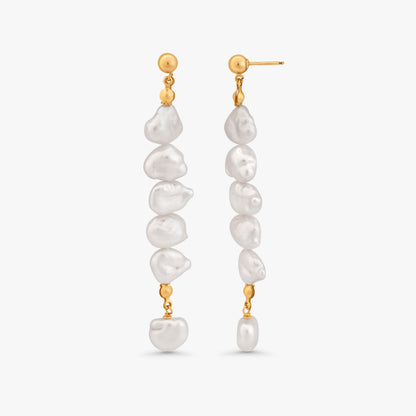 A pair of gold dangle earrings with irregular white baroque pearls, shown against a light gray background.