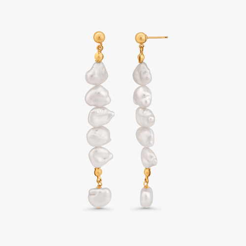 A pair of gold dangle earrings with irregular white baroque pearls, shown against a light gray background.