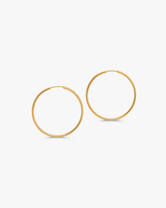 A pair of thin gold hoop earrings shown on a clean, light gray background.
