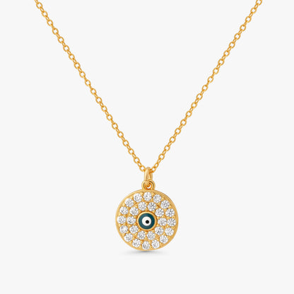 A gold chain necklace with a circular evil eye pendant, featuring clear pavé stones and a small green and white eye detail in the center, set against a light gray background.
