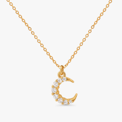 A gold chain necklace with a crescent moon pendant adorned with small clear stones, shown against a light gray background.