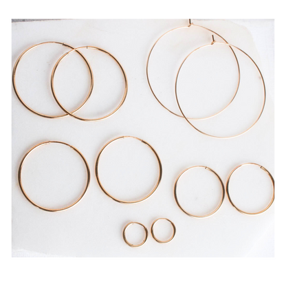 Multiple sizes of 14k gold filled Nia sleeper hoop earrings on white background