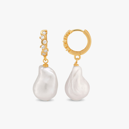 A pair of gold huggie hoop earrings with a vertical bareloeus pearl dangle and a small row of clear cubic zirconia stones, shown on a light gray background.
