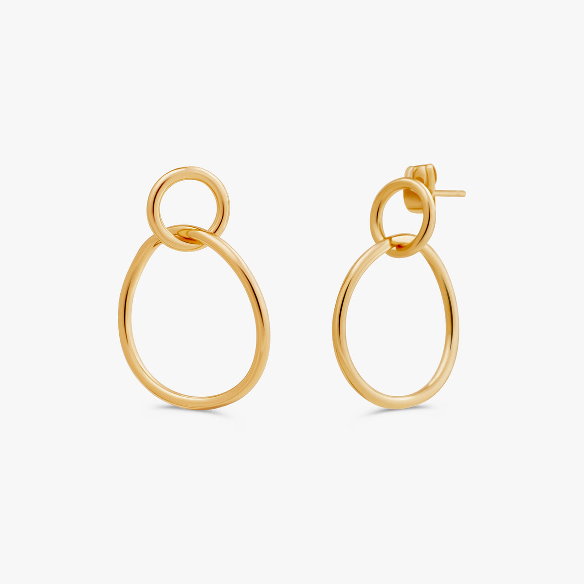 A pair of gold-toned drop earrings with a large oval and a smaller interlocking ring, shown on a clean off-white background.