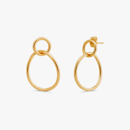 A pair of gold-toned drop earrings with a large oval and a smaller interlocking ring, shown on a clean off-white background.