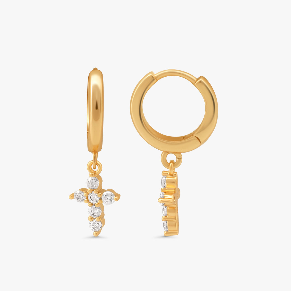 A pair of gold huggie hoop earrings with dangling cross charms set with clear crystals, shown on a light gray background.