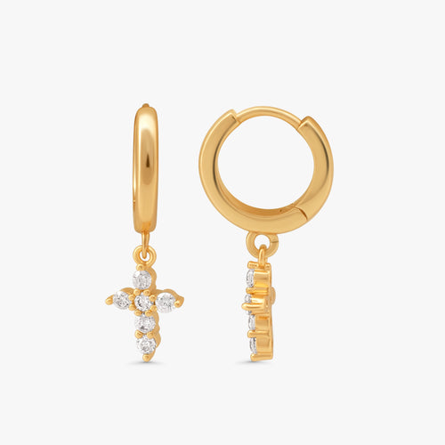 A pair of gold huggie hoop earrings with dangling cross charms set with clear crystals, shown on a light gray background.