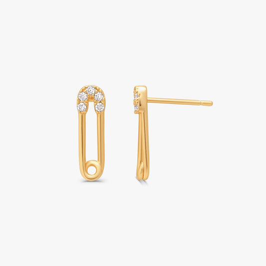 A pair of gold safety-pin stud earrings with a small cluster of clear stones at the top, shown on a light gray background.