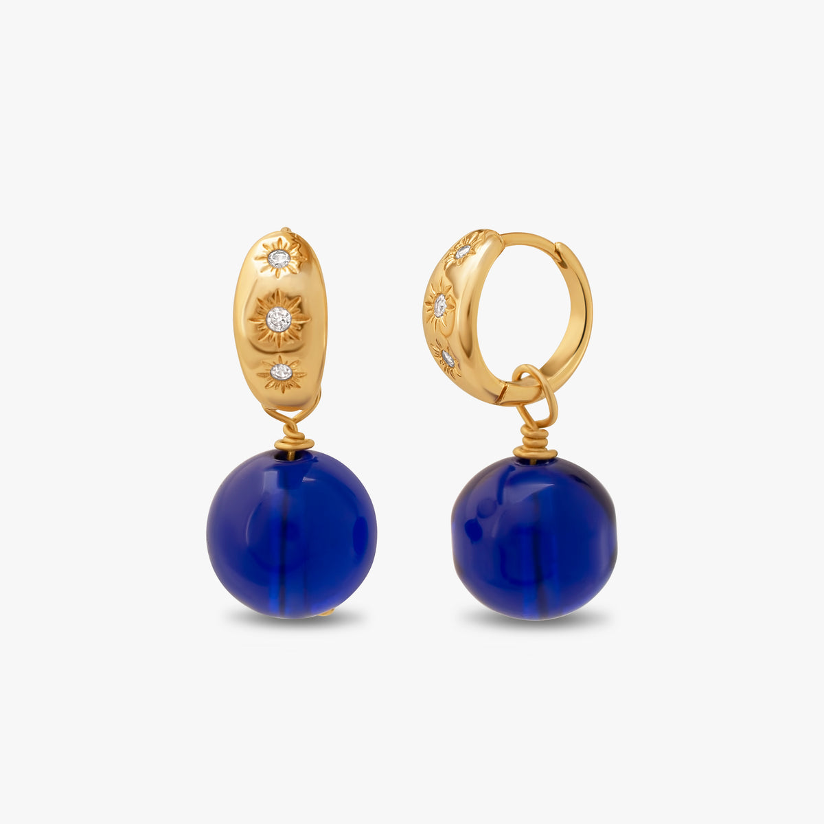 Pair of women's 14k gold-plated huggie hoop earrings with starburst crystal engravings and royal blue sphere bead dangles.