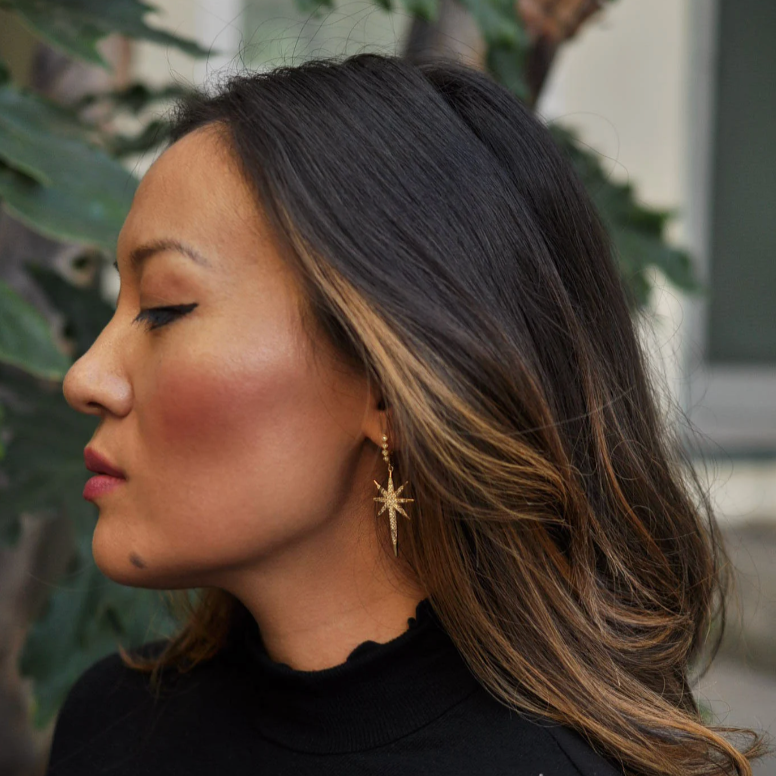 Profile view of woman with dark hair wearing a gold starburst dangle earring.