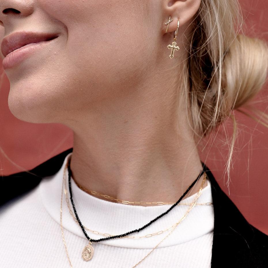 Woman smiling while wearing a 14k Solid Gold cross hoop earring and layered choker necklaces.