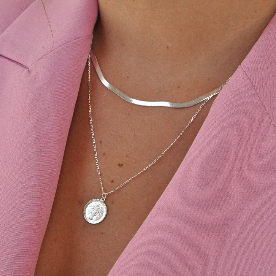 Woman wearing Gioia 925 sterling silver herringbone and Mary medallion necklace set over pink blazer