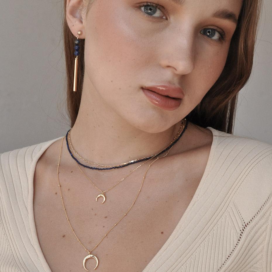Woman wearing Ro Horn 14k gold filled satellite chain necklace layered with delicate gold chains in cream top