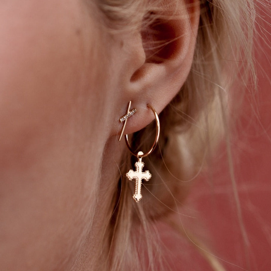 Woman wearing a 14k Solid Gold cross charm hoop earring paired with a upper ear stud.