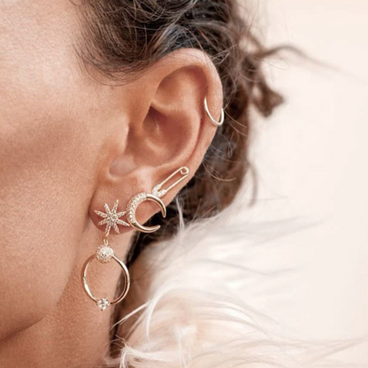 Woman wearing a gold safety pin stud, star drop earring, and crescent moon stud.