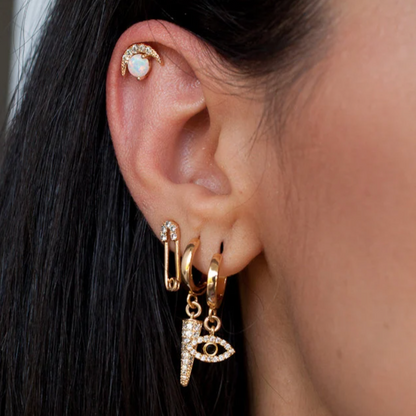Woman wearing an extensive gold ear stack with safety pin stud, evil eye charm hoop, and spike dangle.