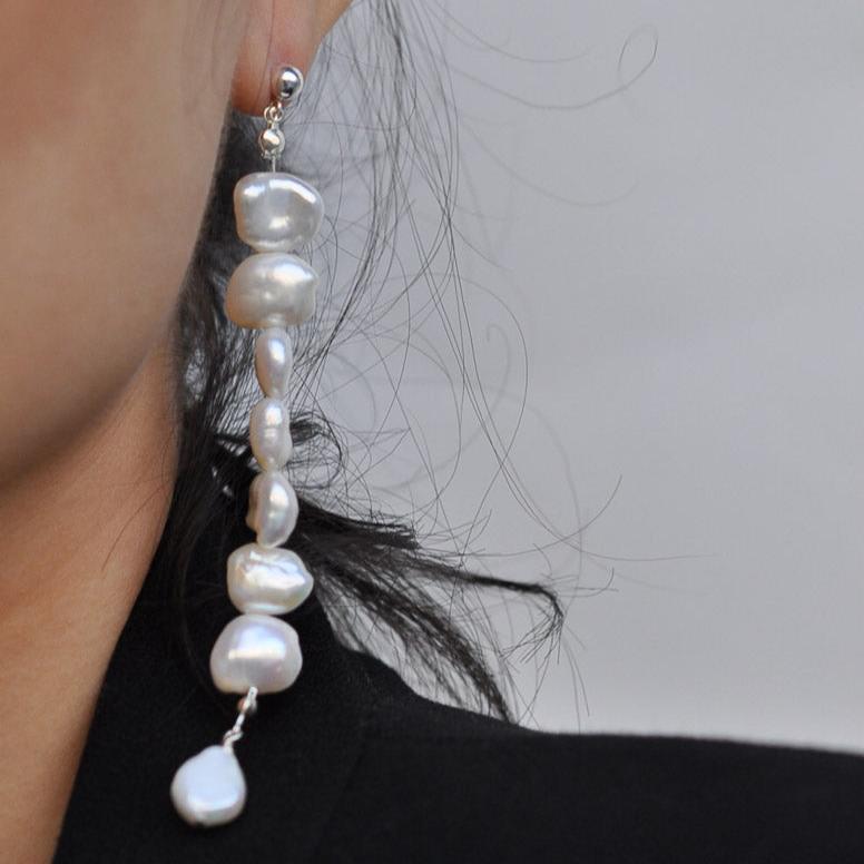 Woman with dark hair wearing long Sterling Silver stacked freshwater pearl drop earrings.