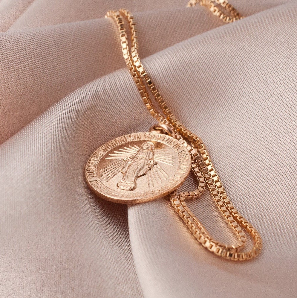 Angled view of Annika Mary 14k gold plated box chain and Virgin Mary charm on draped fabric