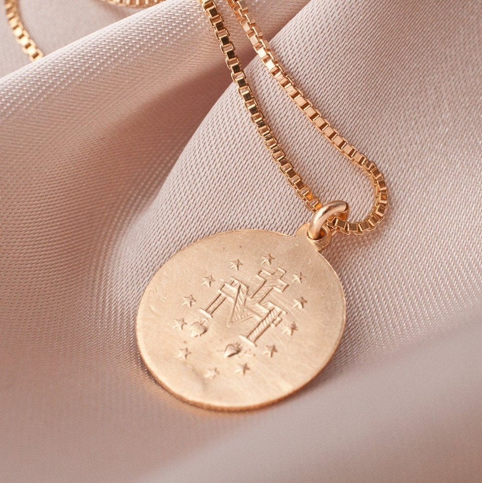 Annika Mary 14k gold plated round medallion pendant displayed flat on soft pink fabric