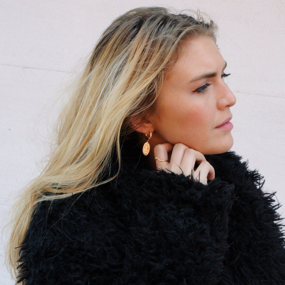 Blonde woman in a black jacket touching her hair while wearing 14k Gold Filled Amara Mary Hoops.