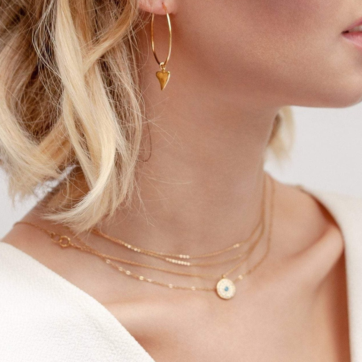 Blonde woman wearing Elin Round Evil Eye 14k gold filled necklace layered with delicate gold chains
