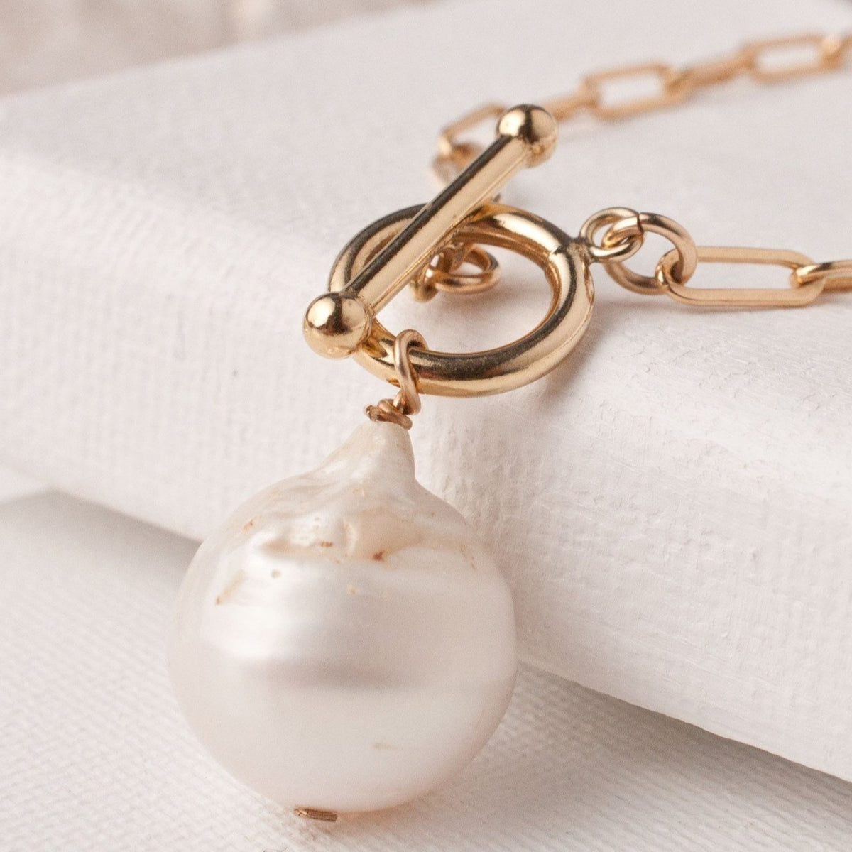 Close-up of Embla Chunky Pearl 14k gold filled toggle clasp and baroque pearl drop resting on light surface