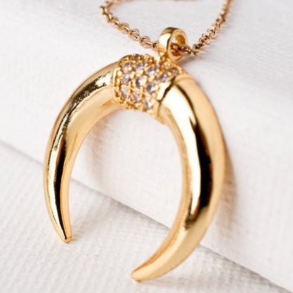 Close-up of Fara Double Horn Tusk 14k gold filled crescent pendant with crystal accents on white surface