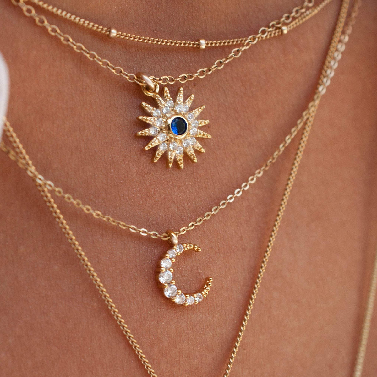 Close-up of Sunniva Sun Ray & Starburst 14k gold filled necklace layered with delicate chain and crescent moon pendant