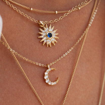 Close-up of Sunniva Sun Ray & Starburst 14k gold filled necklace layered with delicate chain and crescent moon pendant