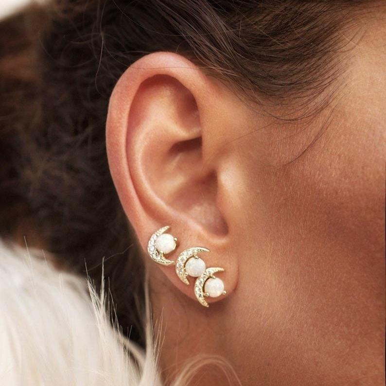Close-up of a woman's ear featuring 14k Gold Plated Tuva Opal Moon Studs stacked in triple lobe piercings.