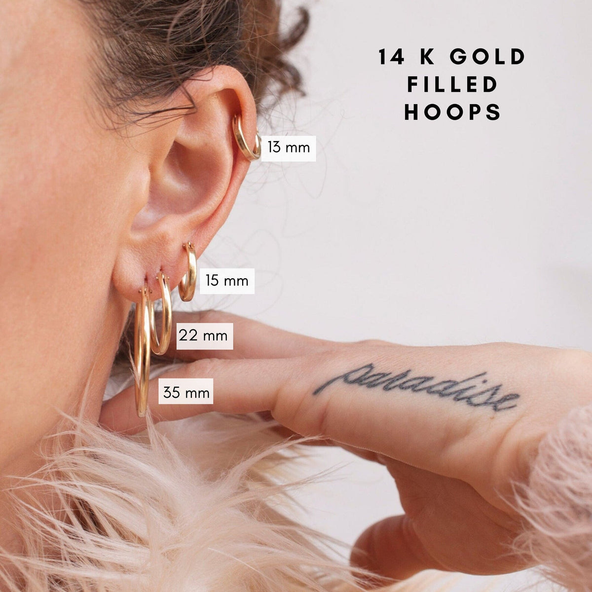 Close-up of a woman touching her ear while displaying 14k Gold Filled Zola Hoop Earrings and size measurements.