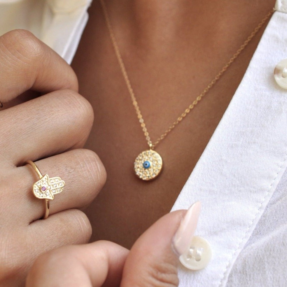 Close-up of woman holding collar while wearing Elin Round Evil Eye 14k gold filled necklace paired with hamsa ring