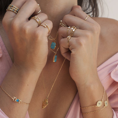 Close-up of woman's hands displaying Mohave Turquoise 14k gold filled necklace, rings, and bracelets in pink top