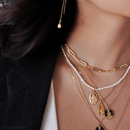 Close-up of woman wearing 14k gold filled Buddha medallion necklace layered with gold chain stack and white top