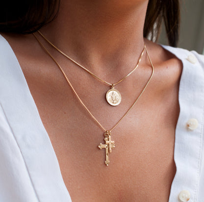 Close-up of woman wearing Annika Mary 14k gold plated medallion necklace layered with cross pendant in white shirt