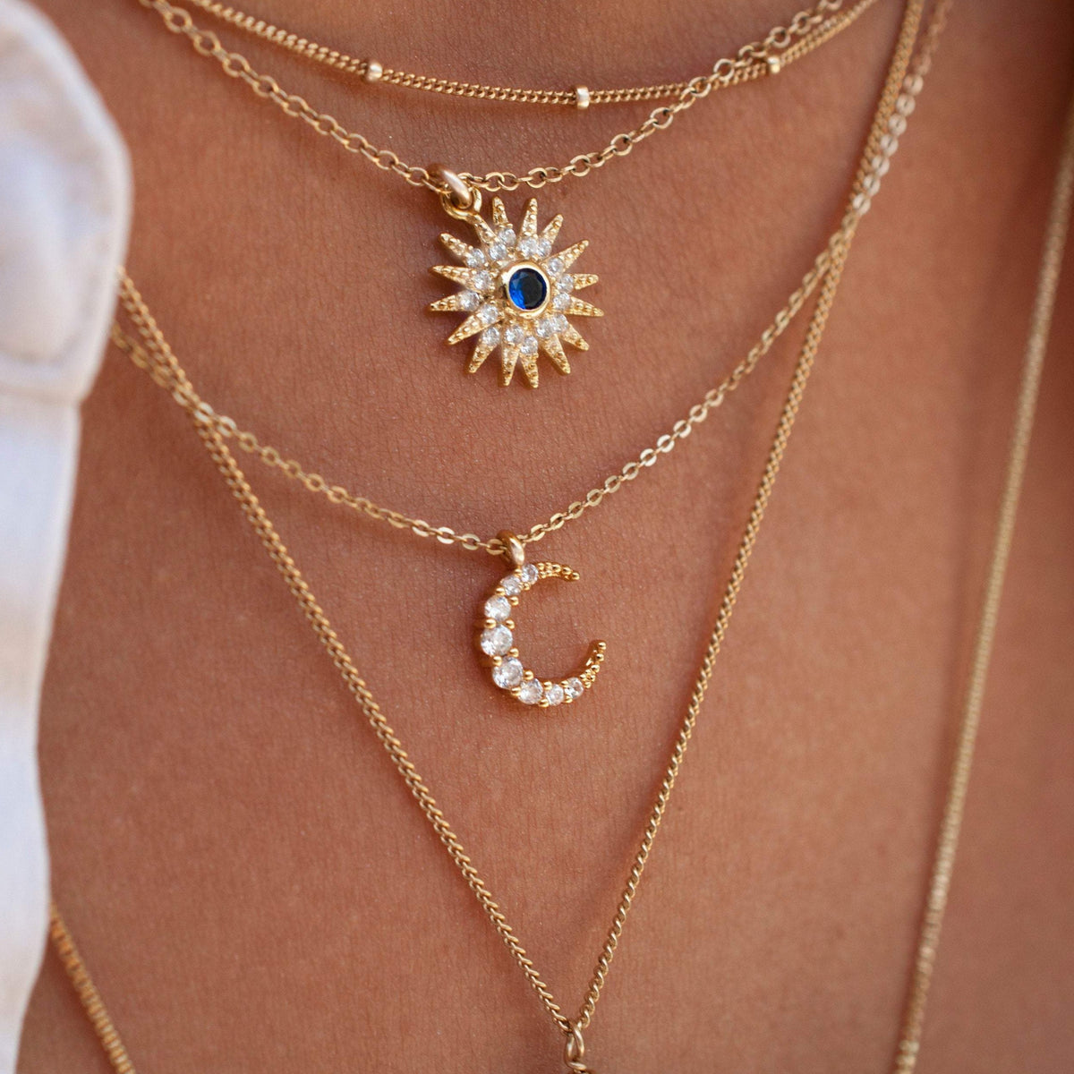 Close-up of woman wearing Maja Mini Moon 14k gold filled crescent necklace layered beneath starburst pendant necklace